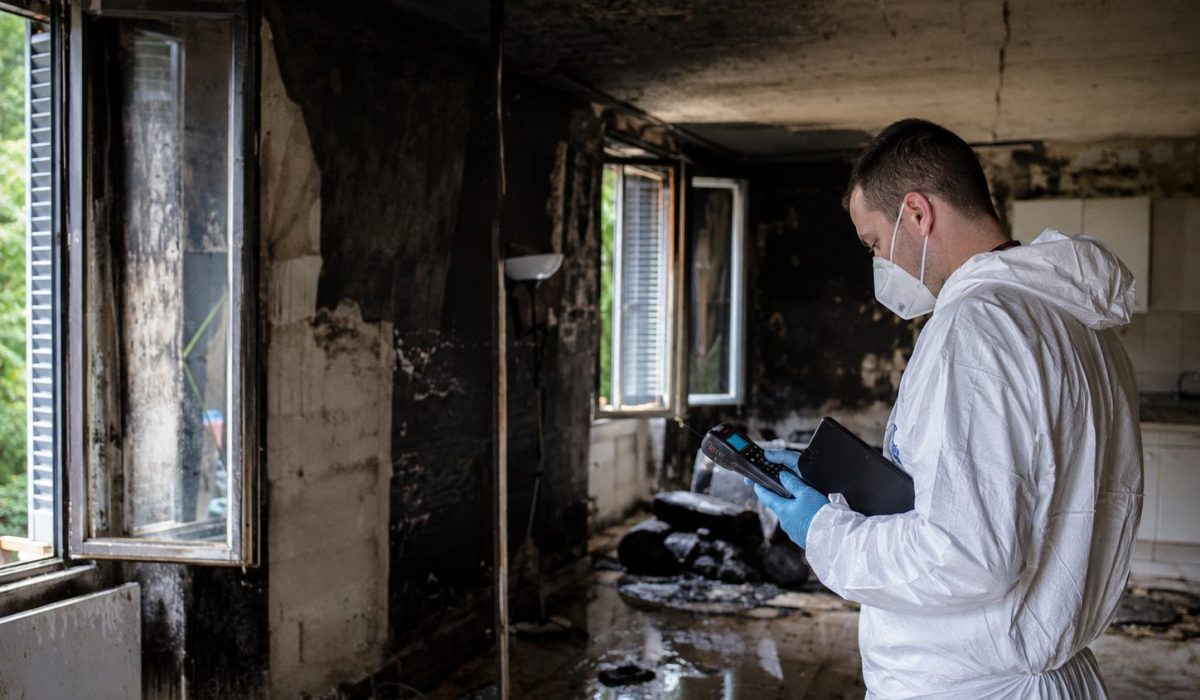 Expert en combinaison de protection contrôlant la salubrité d’un logement après un incendie avec des murs noircis par la fumée et des traces de suie