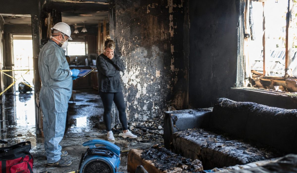 Professionnel en combinaison inspectant les dégâts d’un logement après un incendie avec une habitante inquiète