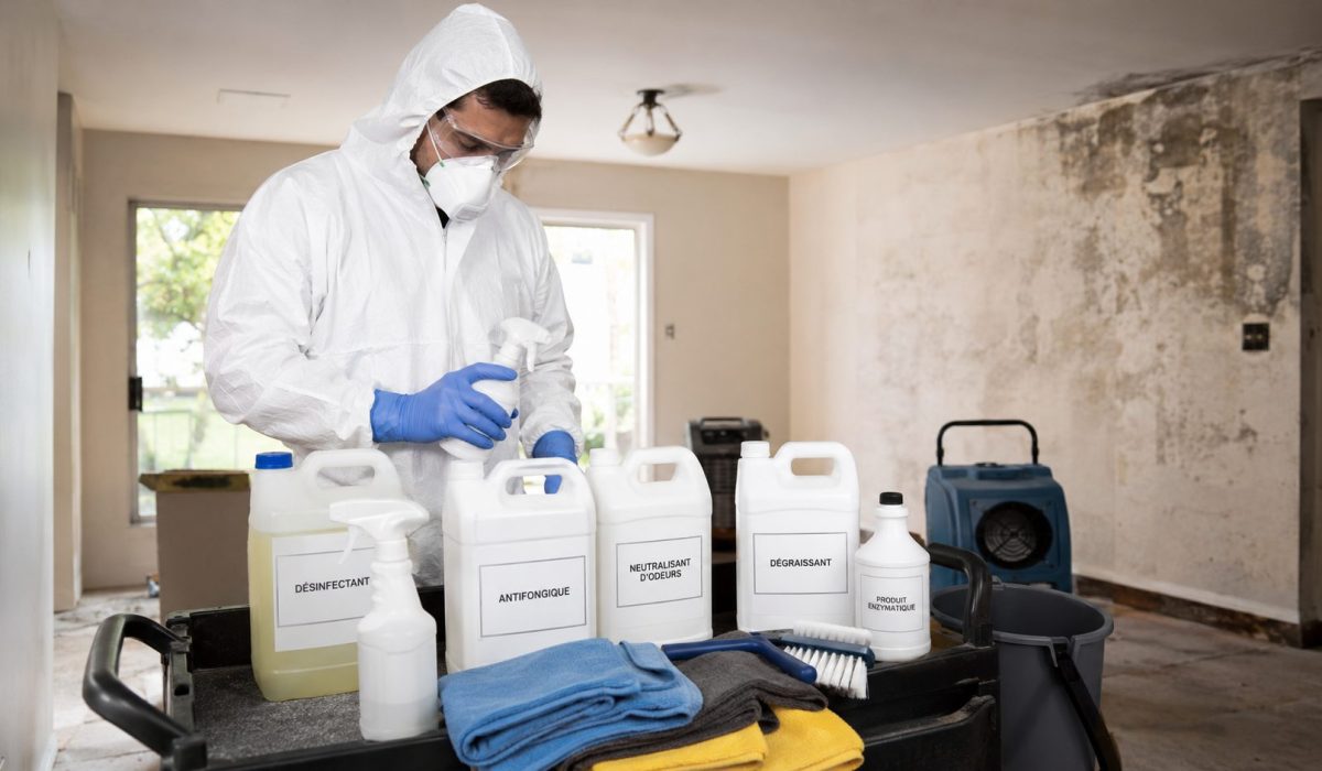Technicien en combinaison de protection préparant des produits de désinfection après un sinistre dans une pièce endommagée par l’humidité