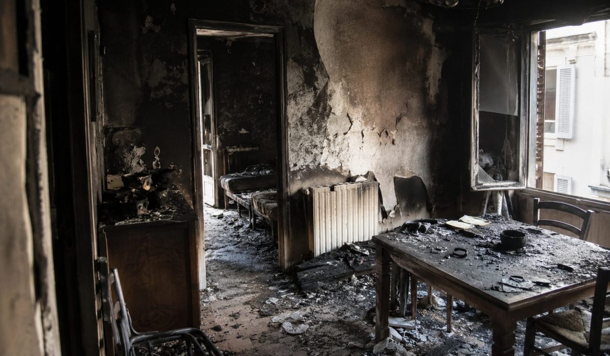 Intérieur d’un logement fortement endommagé par un incendie avec murs noircis, meubles brûlés et débris au sol