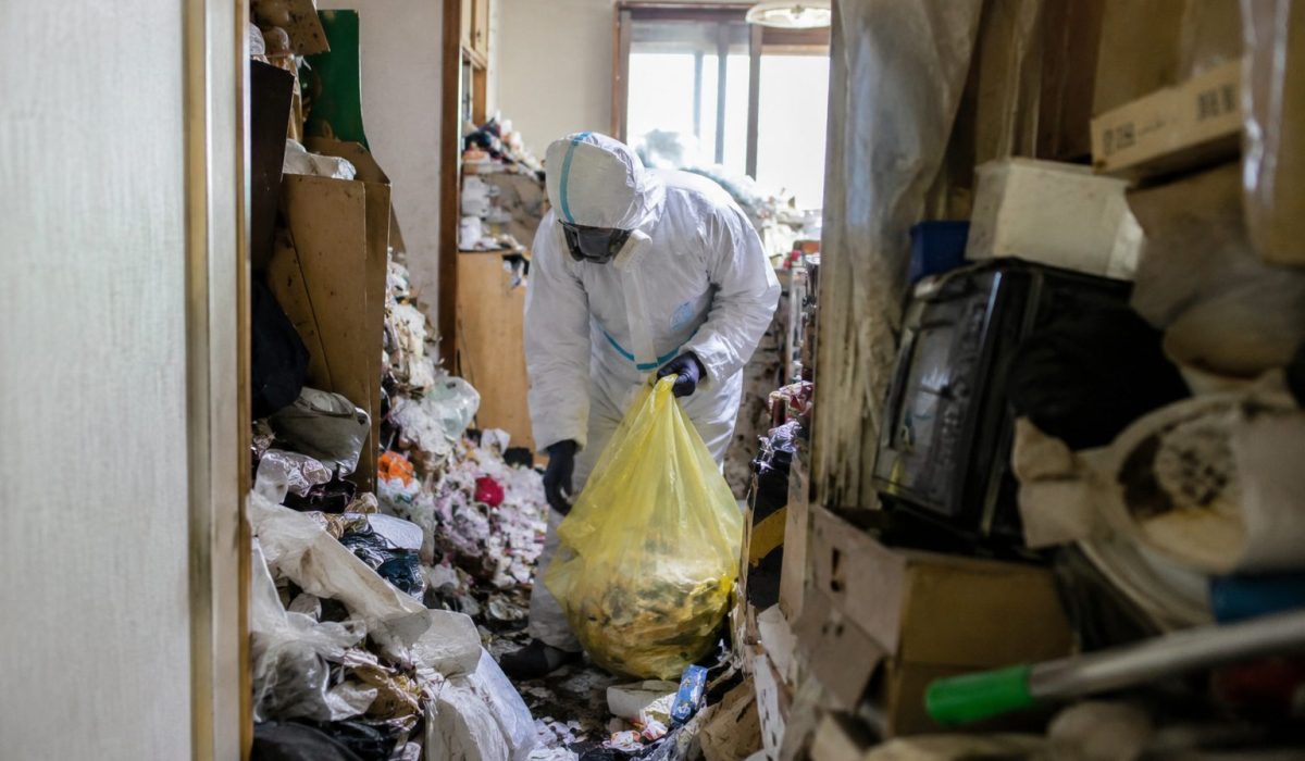 Professionnel en combinaison de protection nettoyant un logement très encombré après un syndrome de Diogène