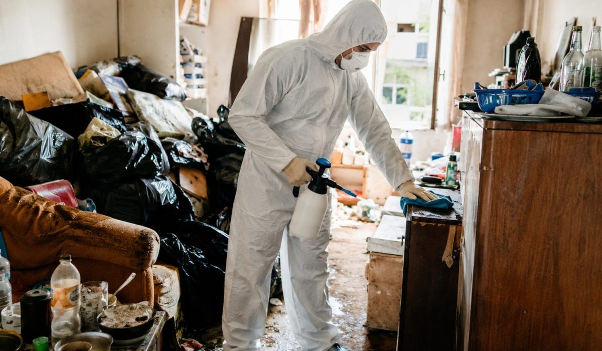 Professionnel en combinaison de protection désinfectant un logement très encombré après un syndrome de Diogène